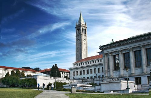 A scenic view of the sather tower and adjacent classical buildings at the university of california, berkeley campus under a blue sky with light clouds.