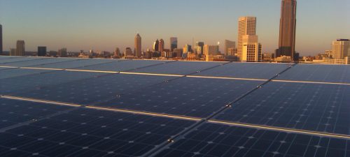 Solar panels covering a rooftop with a city skyline in the background during sunset.