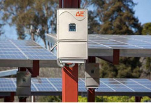 Inverter mounted on a pole with solar panels in the background, under a clear sky.