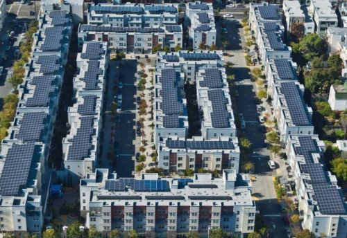 Aerial view of a modern residential complex with numerous buildings covered in solar panels.