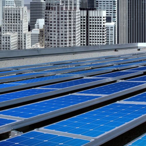 Solar panels installed on a rooftop with a backdrop of skyscrapers in an urban setting.