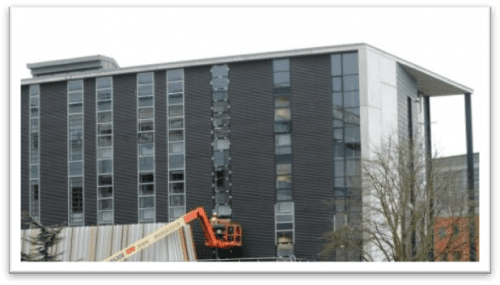 Modern gray office building with a large cherry picker extended towards one side, set against a cloudy sky.