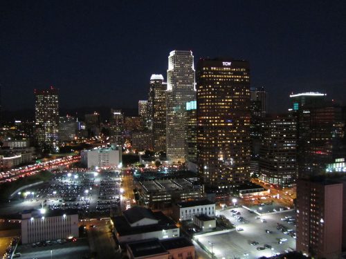 Nighttime cityscape featuring illuminated skyscrapers and busy streets. the foreground shows a large parking area.
