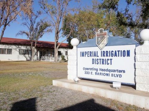 Sign for the imperial irrigation district operating headquarters in front of a building with trees and a clear sky.