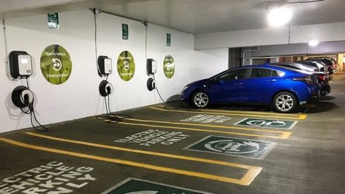 Electric vehicle charging station in a parking garage with a blue car plugged into one of the several available charging points.