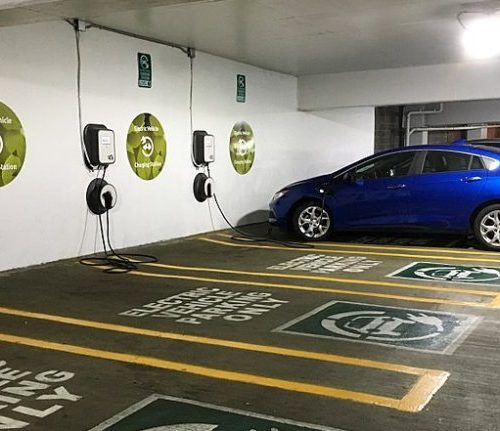 Electric vehicle charging station in a parking garage with a blue car plugged into one of the several available charging points.
