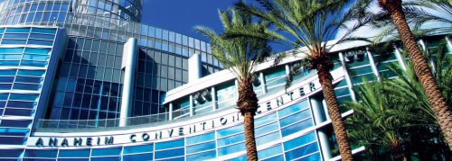 Modern glass facade of the anaheim convention center with tall palm trees in the foreground under a clear blue sky.