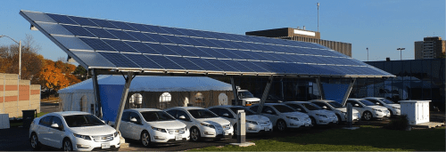 Solar panels mounted above a parking lot full of cars, providing shade and generating renewable energy on a sunny day.