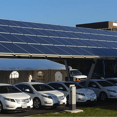 Solar panels mounted above a parking lot full of cars, providing shade and generating renewable energy on a sunny day.