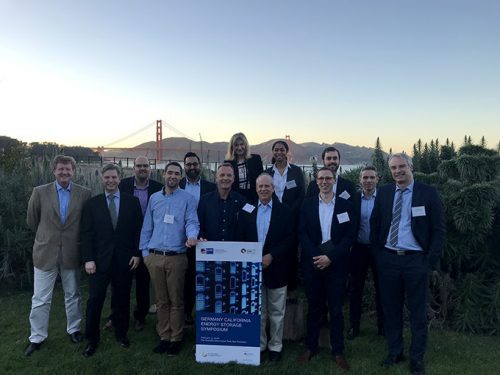 Group of people posing with a conference banner, golden gate bridge in the background during evening.