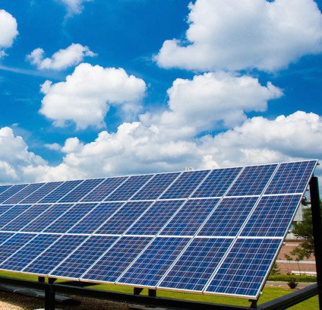 A row of solar panels under a blue sky with fluffy white clouds, capturing solar energy.