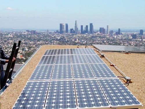 Solar panels on a rooftop with a distant view of a city skyline under a clear sky.