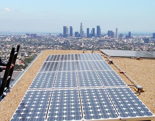 Solar panels on a rooftop with a distant view of a city skyline under a clear sky.
