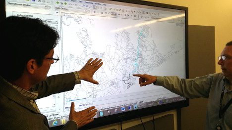 Two men discussing a digital map displayed on a computer screen, pointing and gesturing towards the screen.