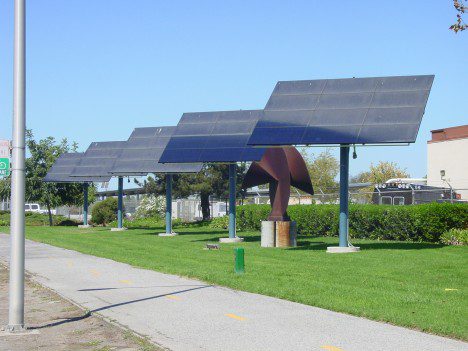 Solar panels mounted on a large metal structure beside a pathway in a sunny park setting.