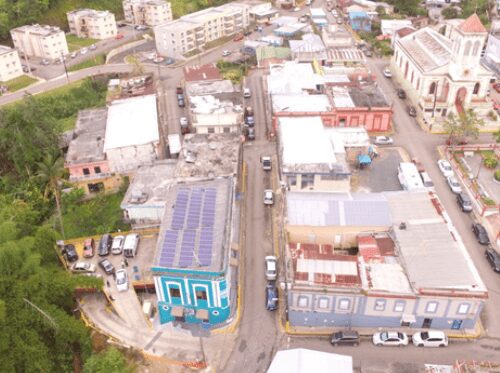 Aerial view of a small town with various buildings, including a church, close-knit residential and commercial structures, and a parking area.