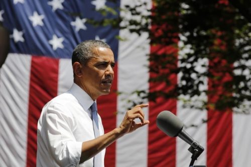 A man in a white shirt and tie speaks at a podium with an american flag in the background.