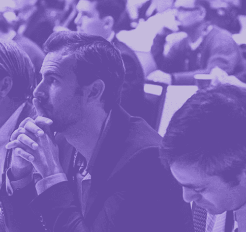 Audience members listening intently at a conference, tinted in purple.