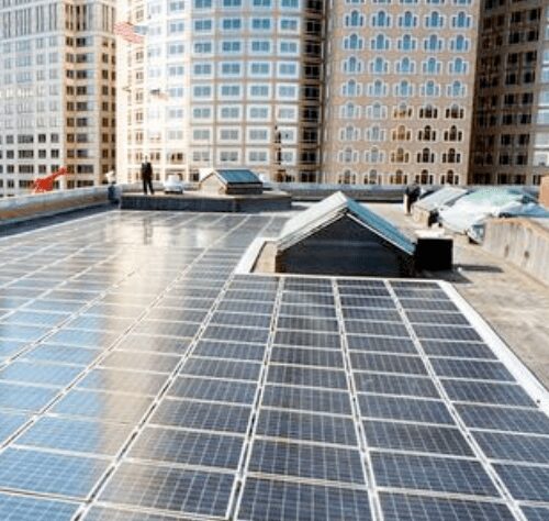 Rooftop covered with solar panels with urban high-rise buildings in the background and a person walking in the distance.