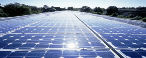 An expansive array of solar panels installed on a large flat roof under clear blue skies.