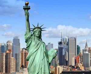 Statue of liberty in the foreground with the new york city skyline in the background under a clear blue sky.