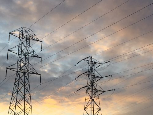 Electrical transmission towers with multiple wires against a sunset sky with clouds.