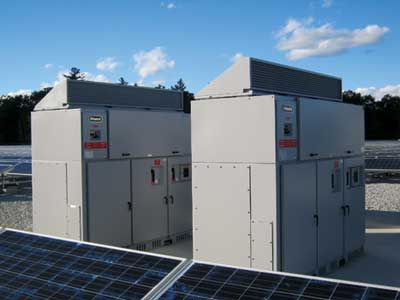 Two industrial electrical inverters on a solar power site under a clear blue sky.