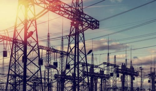 Sunset at an electrical substation with numerous power lines and transformers, highlighting industrial infrastructure against a cloudy sky.