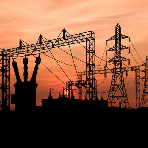 Silhouette of a power plant and electricity pylons against an orange sunset sky.