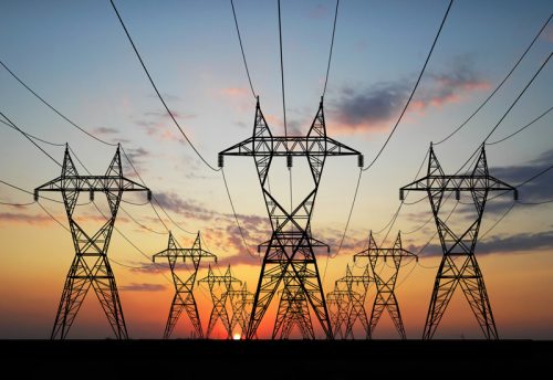 Electricity pylons silhouetted against a sunset, with power lines converging toward the horizon under a colorful sky.