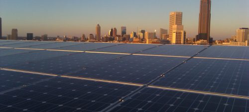 Solar panels cover a rooftop with a city skyline in the background during sunset.