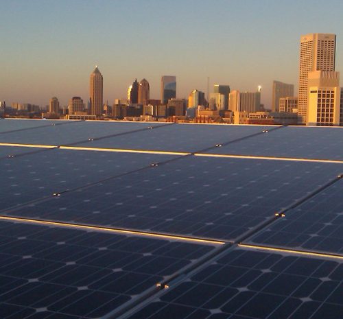 Solar panels cover a rooftop with a city skyline in the background during sunset.