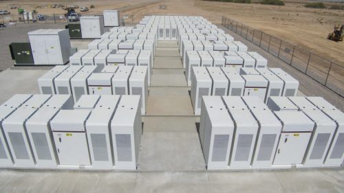Aerial view of an industrial outdoor battery storage facility with rows of large white battery units.