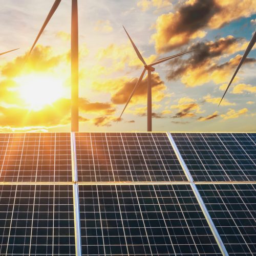 Solar panels and wind turbines under a sunset sky, symbolizing renewable energy.