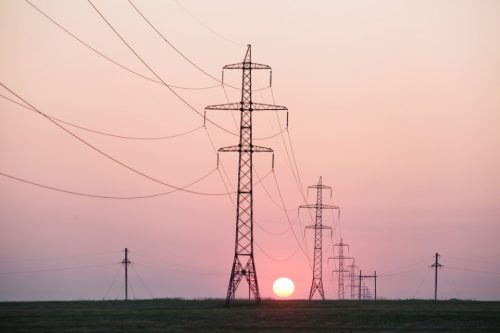 Sunset behind electricity pylons with power lines stretching across a flat landscape.