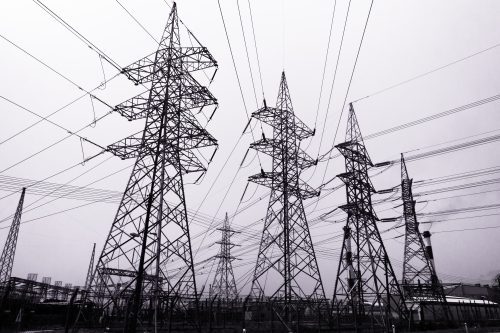 Black and white image of multiple high-voltage electrical transmission towers with an array of power lines against a cloudy sky.