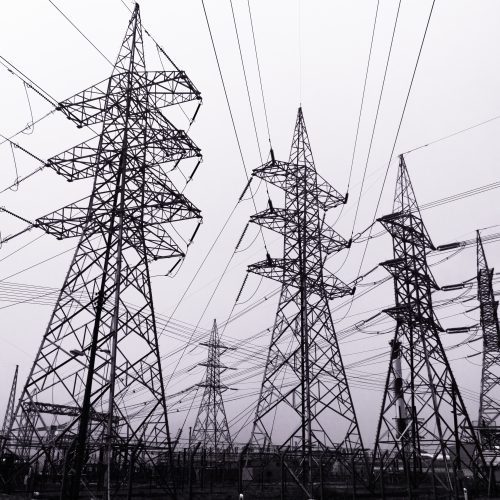 Black and white image of multiple high-voltage electrical transmission towers with an array of power lines against a cloudy sky.
