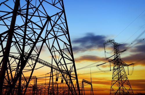 Electricity pylons against a sunset sky with vibrant hues of orange and blue.