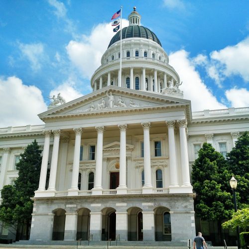 White neoclassical california state capitol building with a large dome and columns, under a blue sky with scattered clouds.