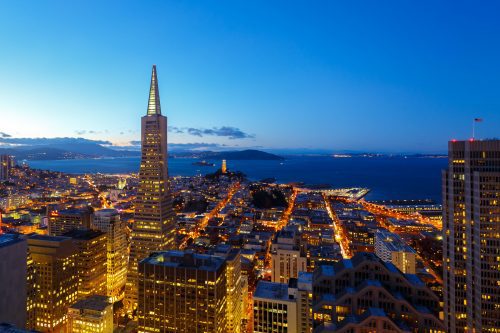 Aerial view of san francisco at dusk showing the transamerica pyramid and city lights, with the bay and alcatraz island in the background.
