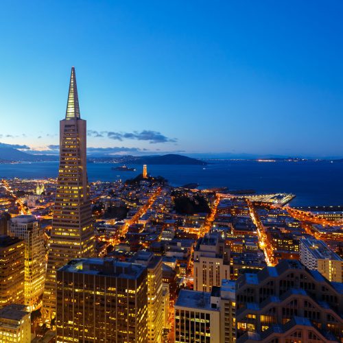 Aerial view of san francisco at dusk showing the transamerica pyramid and city lights, with the bay and alcatraz island in the background.