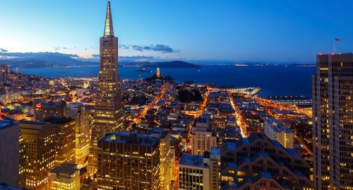 Aerial view of san francisco at dusk, featuring the transamerica pyramid and well-lit city streets leading to the bay.