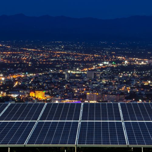Solar panels in the foreground overlooking a brightly lit cityscape at night.