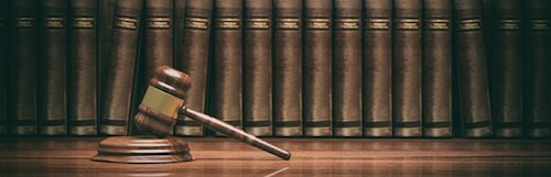 A wooden gavel rests in front of a row of vintage law books in a library setting, symbolizing legal authority.