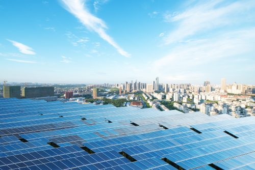 Vast solar panels in the foreground with a panoramic view of a modern city skyline under a clear blue sky.