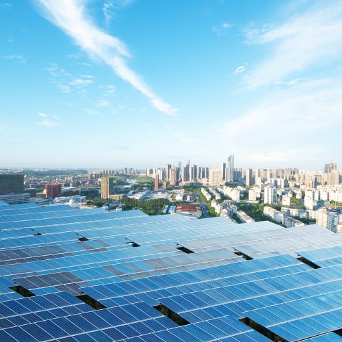 Vast solar panels in the foreground with a panoramic view of a modern city skyline under a clear blue sky.