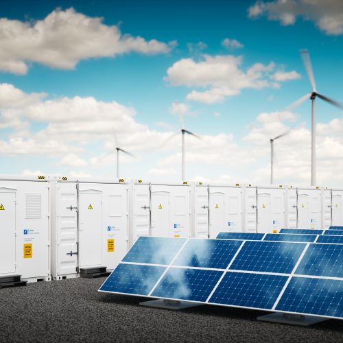 A renewable energy setup with rows of solar panels in the foreground and wind turbines in the back, next to large energy storage units under a blue sky.