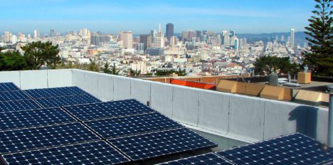 Solar panels on a rooftop with a panoramic view of a city skyline in the background on a clear day.