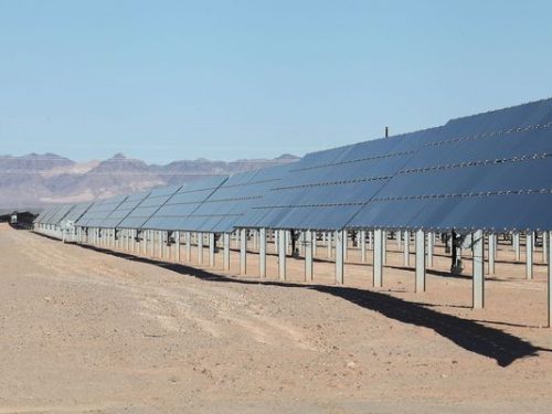 Rows of solar panels in a desert landscape under a clear blue sky.