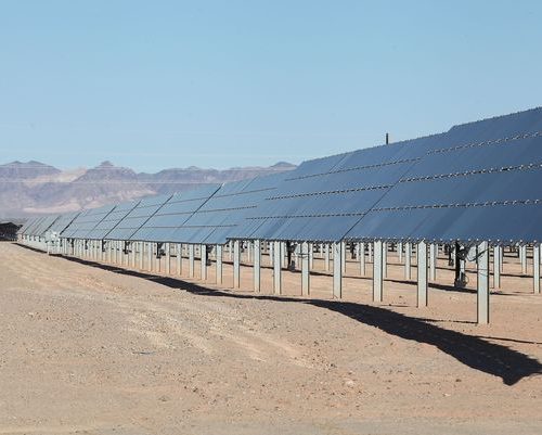Rows of solar panels in a desert landscape under a clear blue sky.
